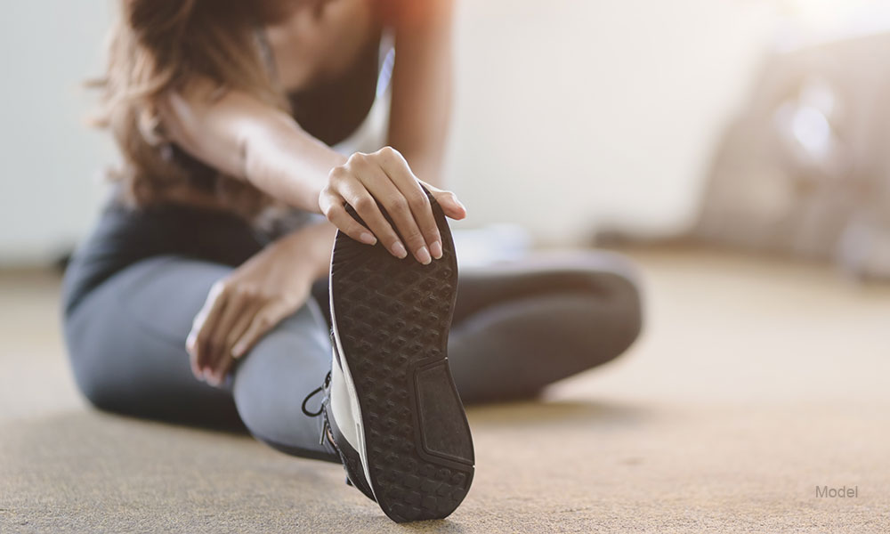 Woman with tan and slim body stretching legs before exercise at the gym